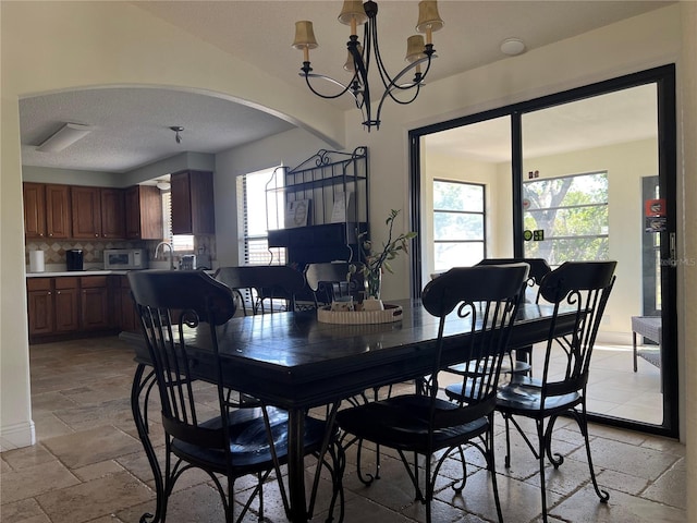 dining area with a textured ceiling, arched walkways, stone tile flooring, and an inviting chandelier