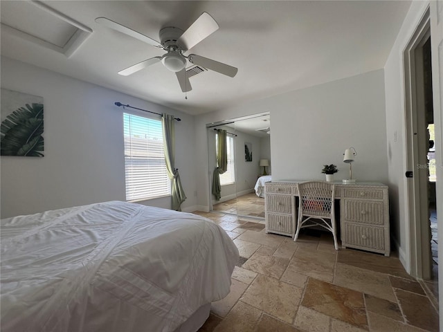 bedroom featuring baseboards, visible vents, ceiling fan, stone tile flooring, and a closet