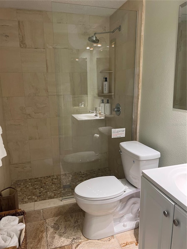 bathroom featuring toilet, a textured wall, tiled shower, and vanity