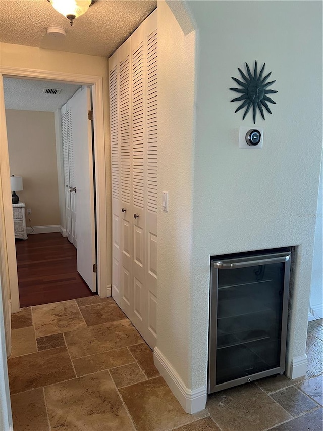 corridor featuring stone tile flooring, baseboards, visible vents, and a textured ceiling