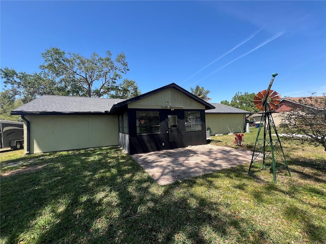rear view of property featuring a lawn, a shingled roof, and a patio area