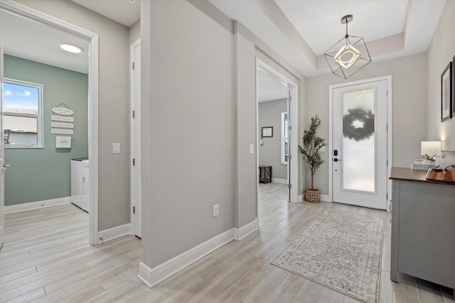 foyer featuring a chandelier, light wood-type flooring, washer and clothes dryer, and baseboards