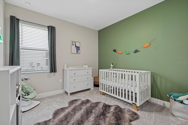 carpeted bedroom featuring baseboards and a nursery area
