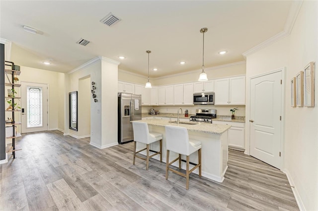 10015 Marbella Dr, Bradenton, FL 34211 - kitchen featuring stainless steel appliances, white cabinets, ornamental molding, light wood-style floors, and an island with sink