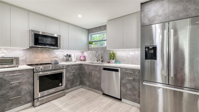 kitchen with a sink, stainless steel appliances, tasteful backsplash, light wood-style flooring, and light countertops