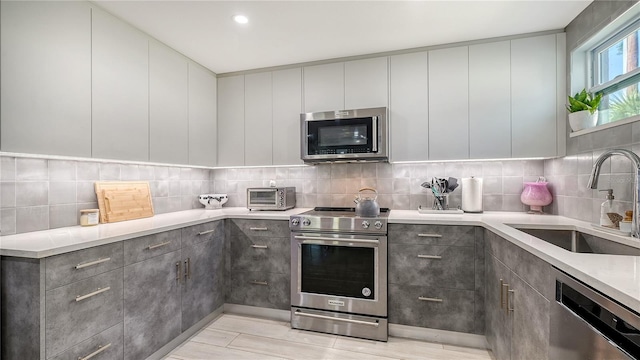 kitchen with a sink, modern cabinets, gray cabinetry, appliances with stainless steel finishes, and decorative backsplash