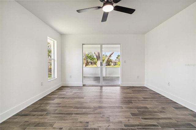 empty room featuring dark wood-type flooring, a ceiling fan, and baseboards