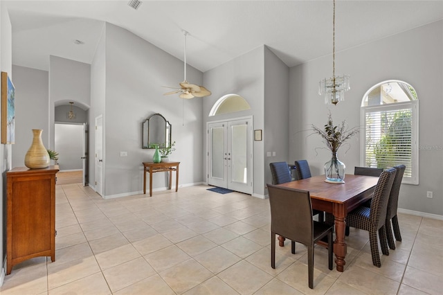 dining room featuring arched walkways, baseboards, ceiling fan with notable chandelier, high vaulted ceiling, and light tile patterned floors