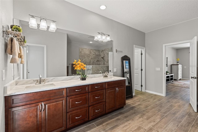 bathroom with double vanity, wood finished floors, tiled shower, and a sink