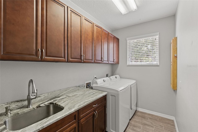 laundry room with a sink, washing machine and dryer, light wood-type flooring, baseboards, and cabinet space