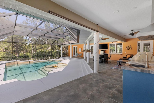 outdoor pool featuring glass enclosure, a ceiling fan, a sink, a patio, and exterior kitchen
