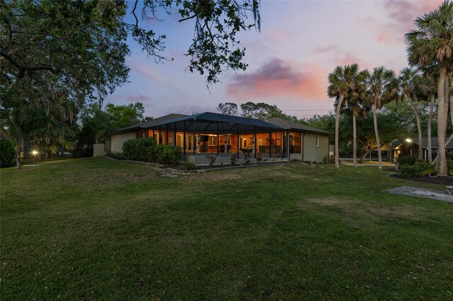 back of property at dusk featuring a lanai and a yard