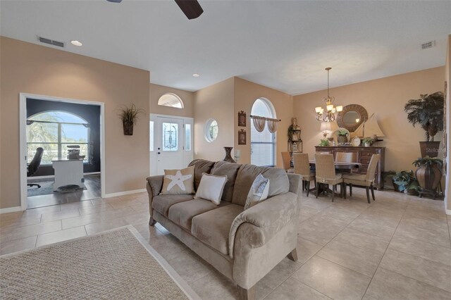 living room featuring ceiling fan with notable chandelier, visible vents, baseboards, and light tile patterned floors