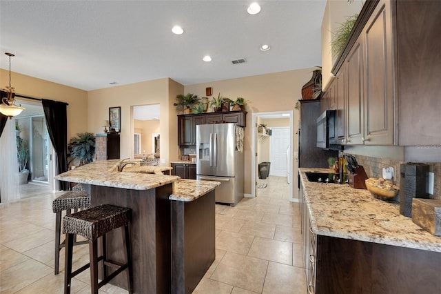 kitchen featuring a breakfast bar area, stainless steel refrigerator with ice dispenser, backsplash, visible vents, and dark brown cabinetry