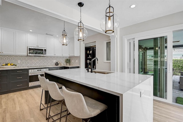 577 Corwood Dr, Sarasota, FL 34234 - kitchen featuring backsplash, a sink, light wood-style flooring, stainless steel appliances, and a kitchen island with sink