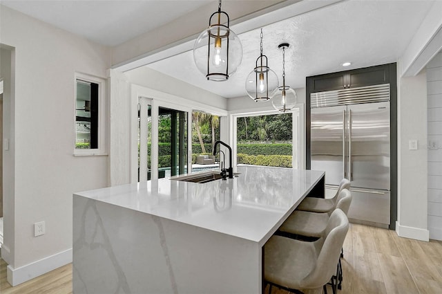 577 Corwood Dr, Sarasota, FL 34234 - kitchen featuring light countertops, stainless steel built in refrigerator, hanging light fixtures, a sink, and light wood-style floors