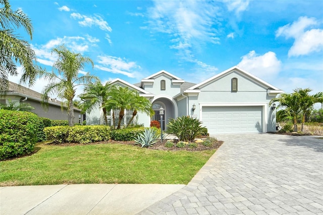 view of front of property with stucco siding, an attached garage, a front lawn, and decorative driveway