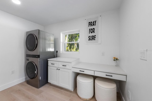 laundry area with baseboards, stacked washer and dryer, cabinet space, and light wood-style flooring