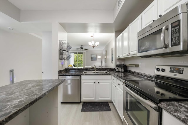kitchen with dark stone countertops, a sink, stainless steel appliances, white cabinets, and a chandelier