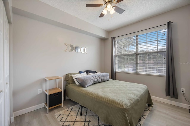 bedroom featuring light wood-style floors, baseboards, ceiling fan, and a textured ceiling