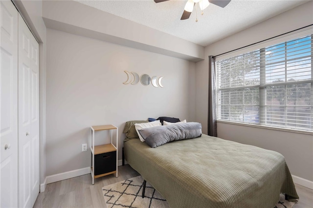 bedroom featuring a closet, a textured ceiling, ceiling fan, light wood-style flooring, and baseboards