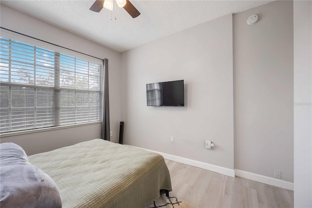 bedroom with a textured ceiling, baseboards, light wood-type flooring, and a ceiling fan