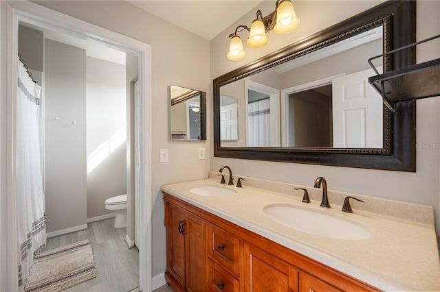 full bathroom with a sink, double vanity, toilet, and baseboards