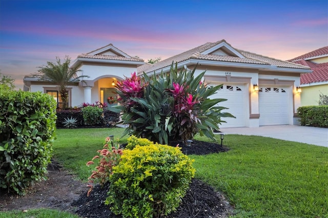 view of front of property with a lawn, a garage, a tile roof, stucco siding, and driveway
