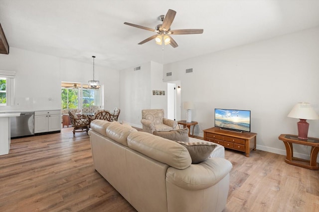 living room featuring vaulted ceiling, ceiling fan with notable chandelier, light wood finished floors, and visible vents