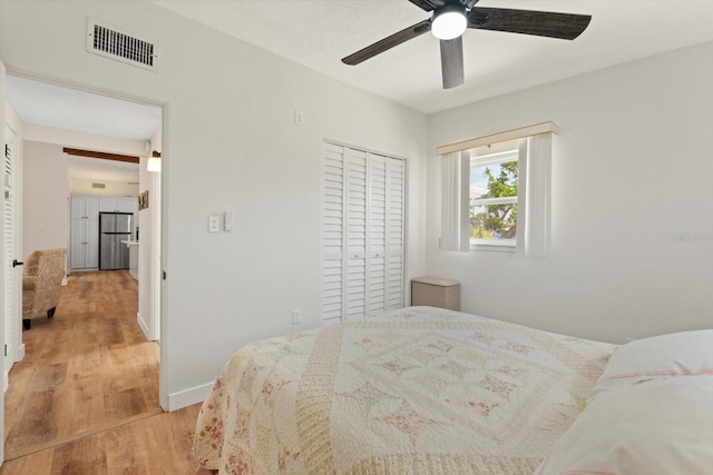 bedroom with baseboards, light wood-style floors, visible vents, freestanding refrigerator, and a closet