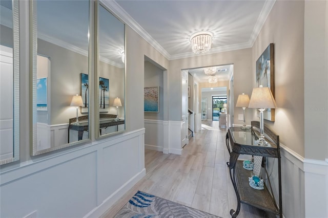 hall with crown molding, light wood-style floors, an inviting chandelier, and a wainscoted wall