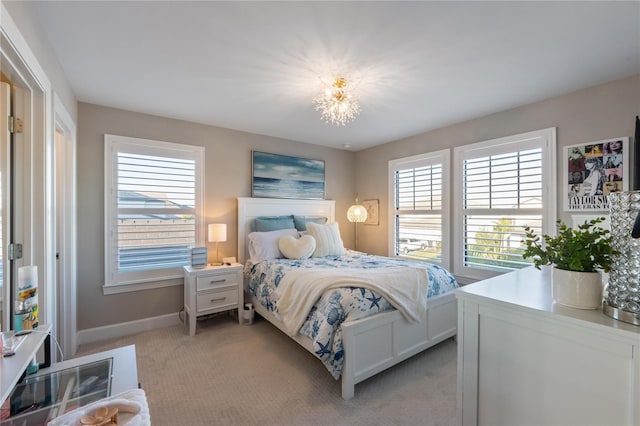 bedroom featuring light colored carpet, an inviting chandelier, and baseboards