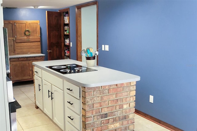 kitchen with light tile patterned floors, white cabinets, baseboards, black electric cooktop, and light countertops