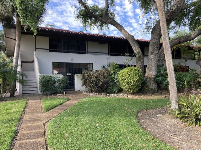 view of front of house with a front lawn, stairs, a tile roof, and stucco siding