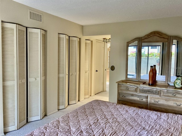 bedroom with a textured ceiling, carpet, multiple closets, and visible vents
