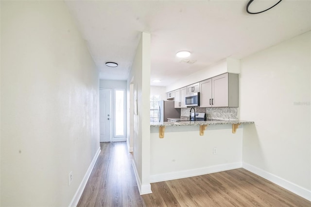 1236 Dovehill Dr, Apopka, FL 32703 - kitchen featuring appliances with stainless steel finishes, a breakfast bar area, light wood-style floors, decorative backsplash, and light stone counters