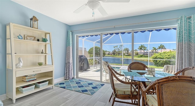 interior space with baseboards, a ceiling fan, light wood-style floors, a water view, and a sunroom