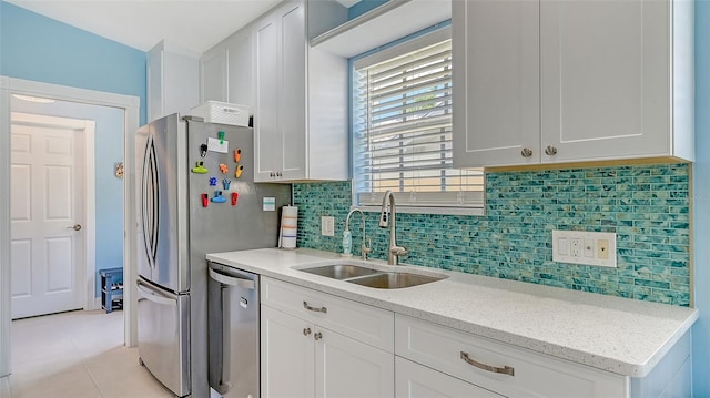 kitchen with white cabinetry, light stone counters, dishwasher, a sink, and decorative backsplash
