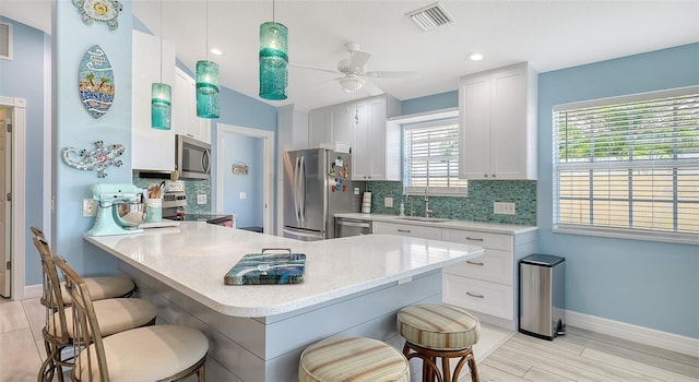 kitchen with visible vents, a sink, a kitchen bar, stainless steel appliances, and backsplash