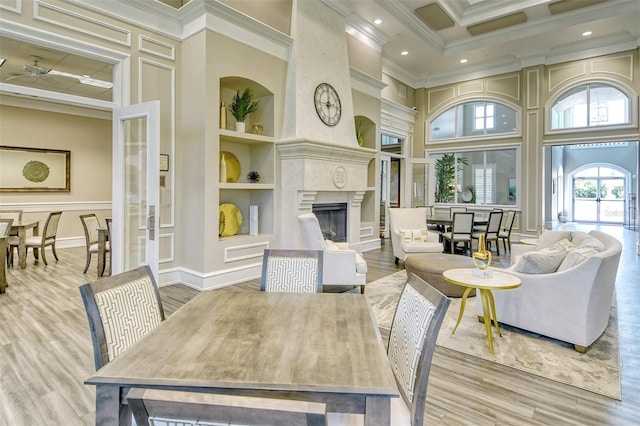 living room featuring a towering ceiling, built in features, crown molding, wood finished floors, and a premium fireplace
