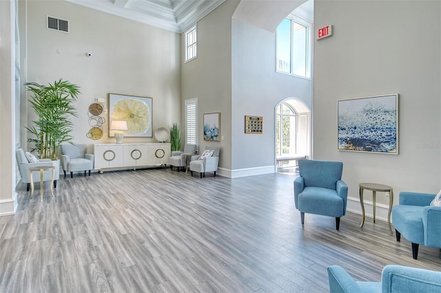sitting room with arched walkways, a towering ceiling, wood finished floors, a healthy amount of sunlight, and baseboards