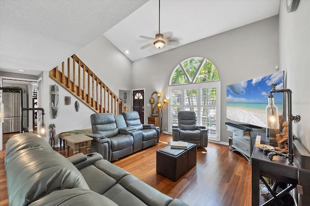 living area featuring a textured ceiling, hardwood / wood-style flooring, ceiling fan, a towering ceiling, and stairway