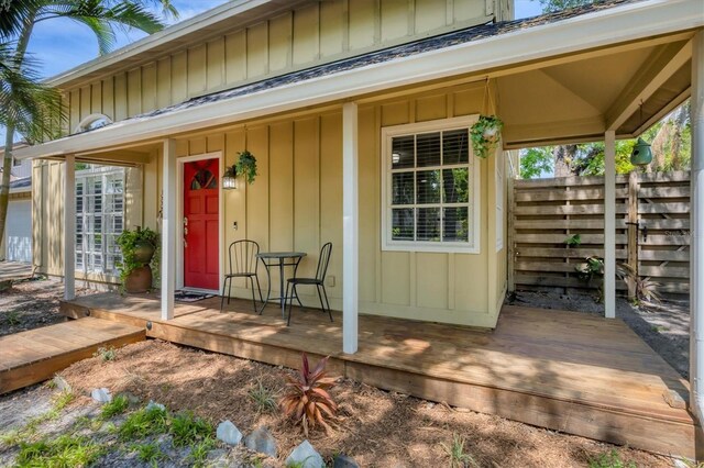 view of exterior entry featuring board and batten siding, a porch, and fence