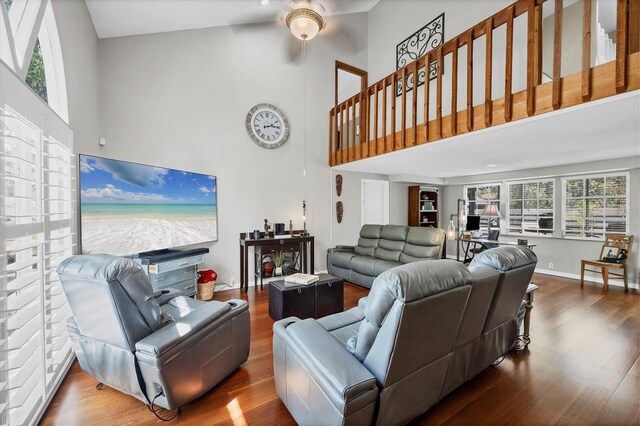 living area with a towering ceiling, baseboards, ceiling fan, and wood finished floors
