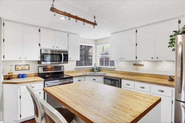 kitchen with a sink, white cabinetry, butcher block countertops, and appliances with stainless steel finishes