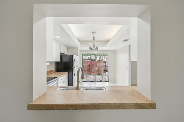 kitchen with white cabinetry, a sink, electric range oven, a tray ceiling, and a notable chandelier