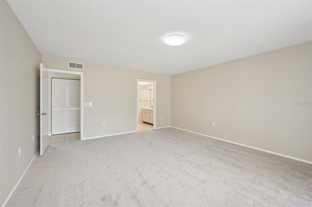 unfurnished bedroom with light carpet, connected bathroom, baseboards, and visible vents