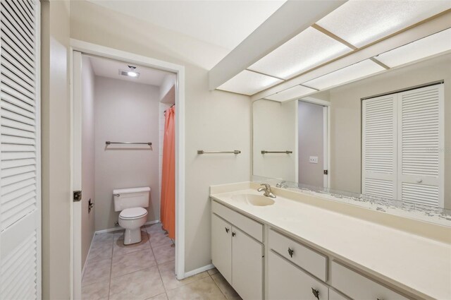 bathroom with a closet, toilet, vanity, tile patterned flooring, and baseboards