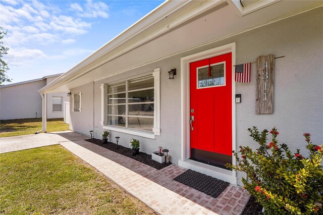 entrance to property with a lawn, a porch, and stucco siding