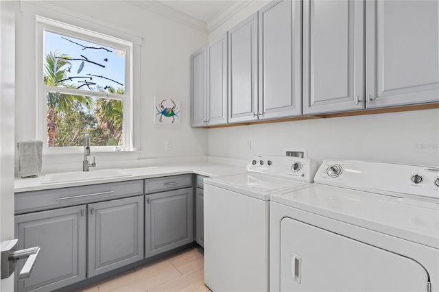 clothes washing area with ornamental molding, washing machine and clothes dryer, a sink, and cabinet space